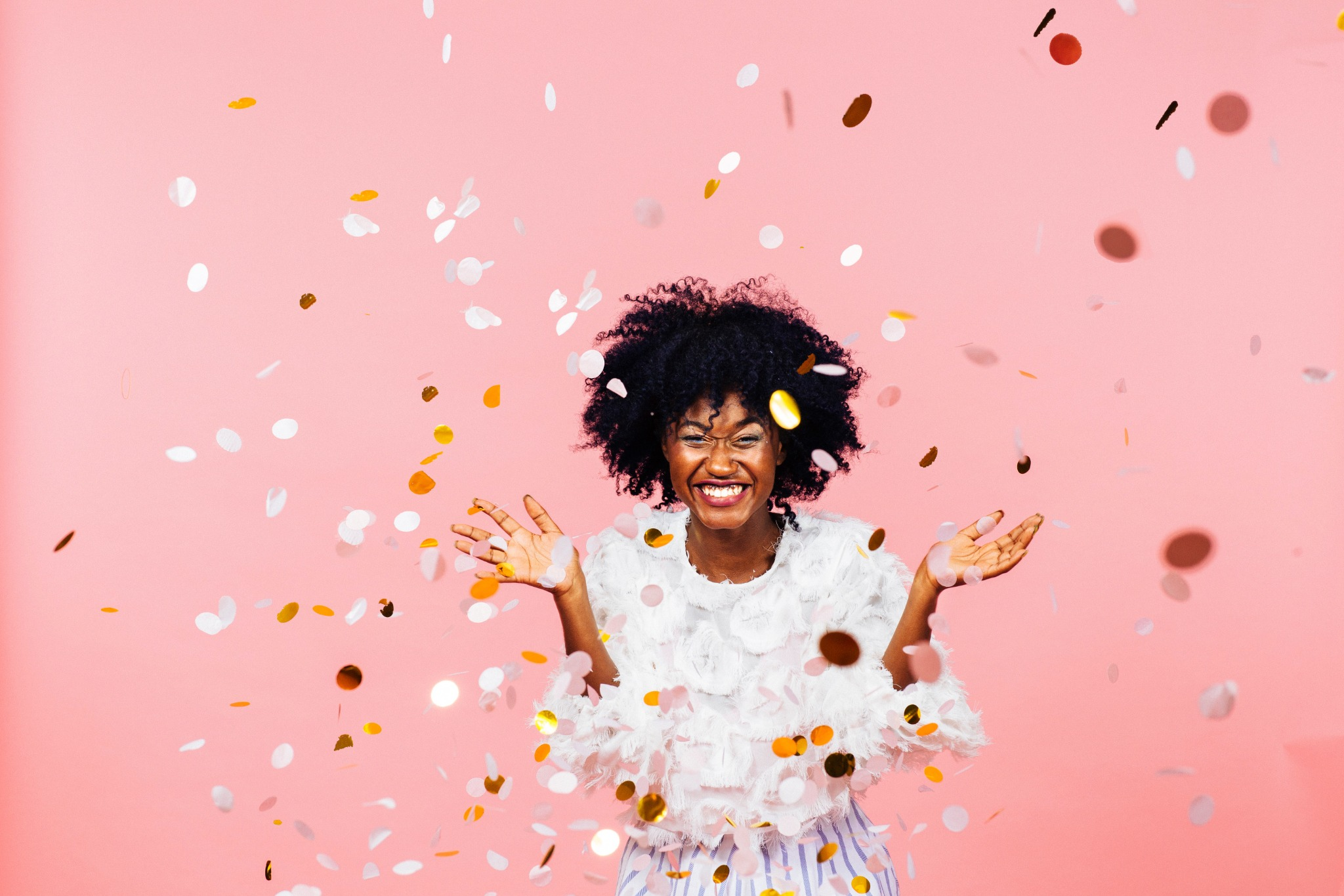A person celebrating against a pink background with confetti falling all around them.