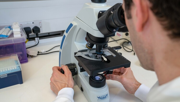 A man looking at a slide on a microscope.